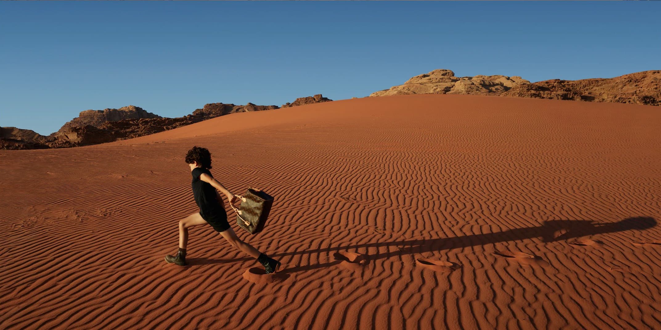 Enfant courant dans les dunes du Wadi Rum avec un sac Louis Vuitton