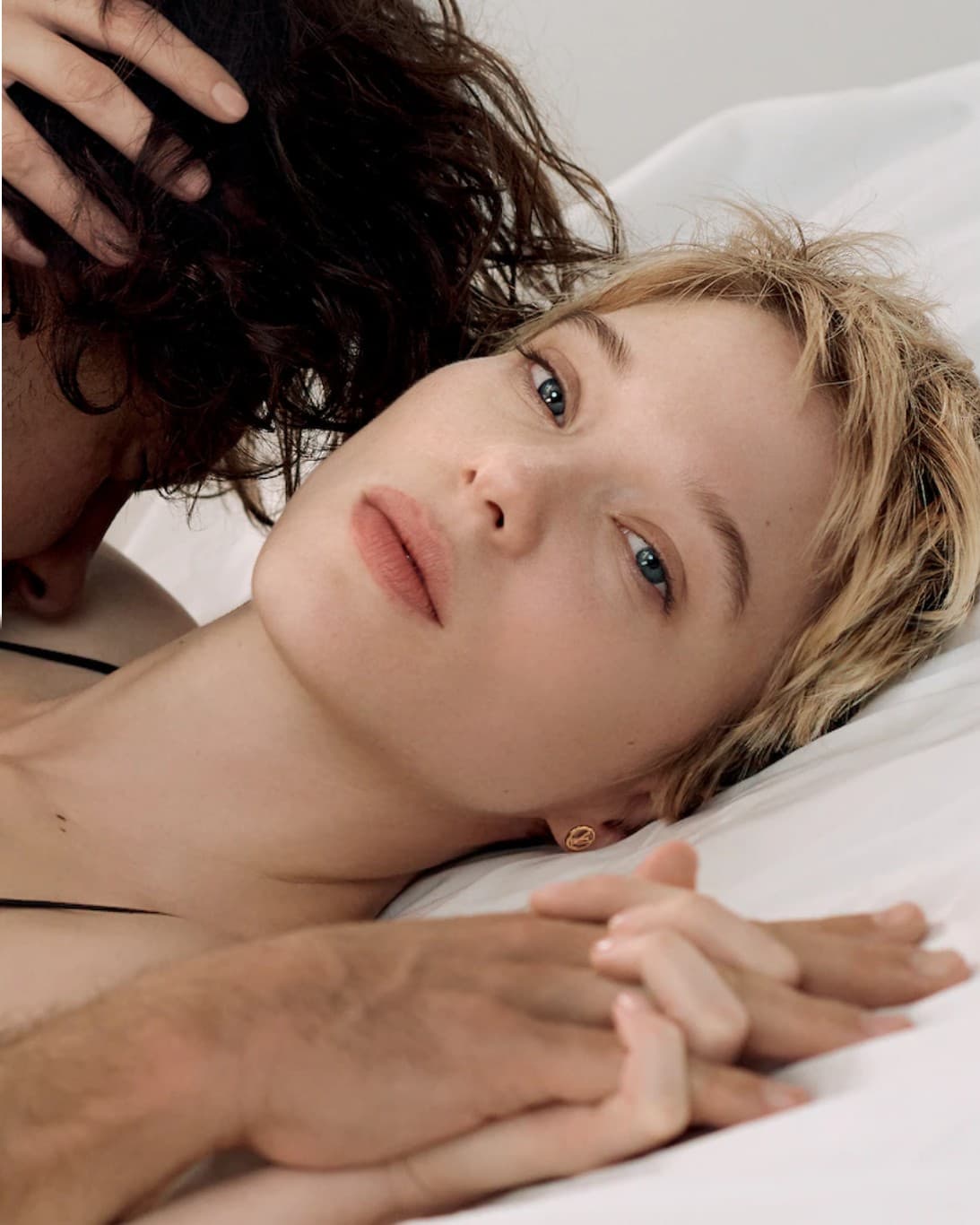 Léa Seydoux allongée, une main dans ses cheveux, leurs mains mêlées
