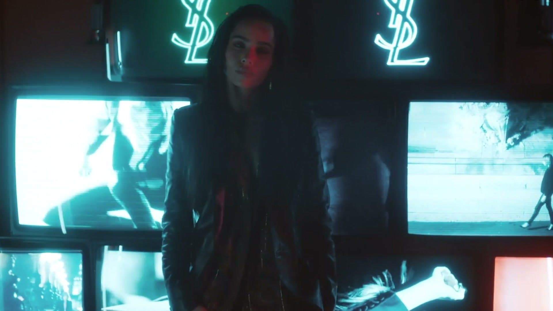 Zoë Kravitz devant un mur d'écrans aux logos YSL